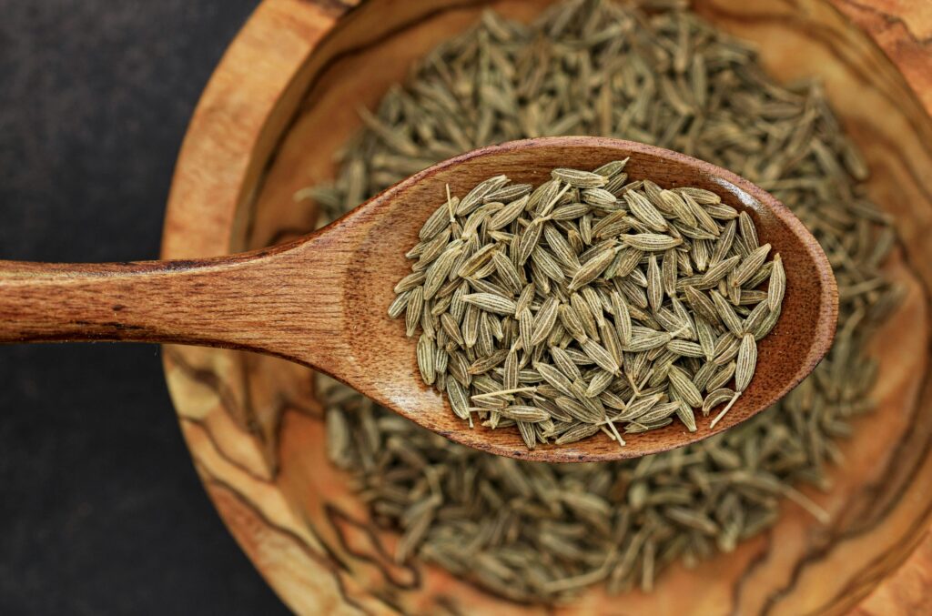 "Close-up of cumin seeds, light brown and elongated, with a ridged texture in brown bowl."